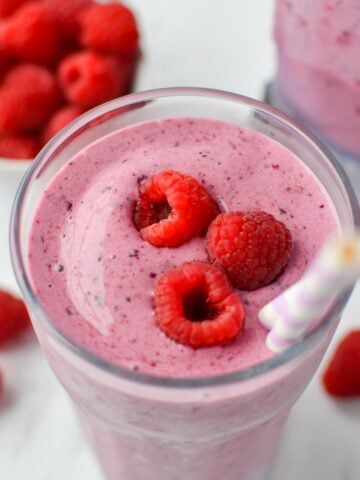 A glass filled with a berry smoothie and topped with fresh raspberries.