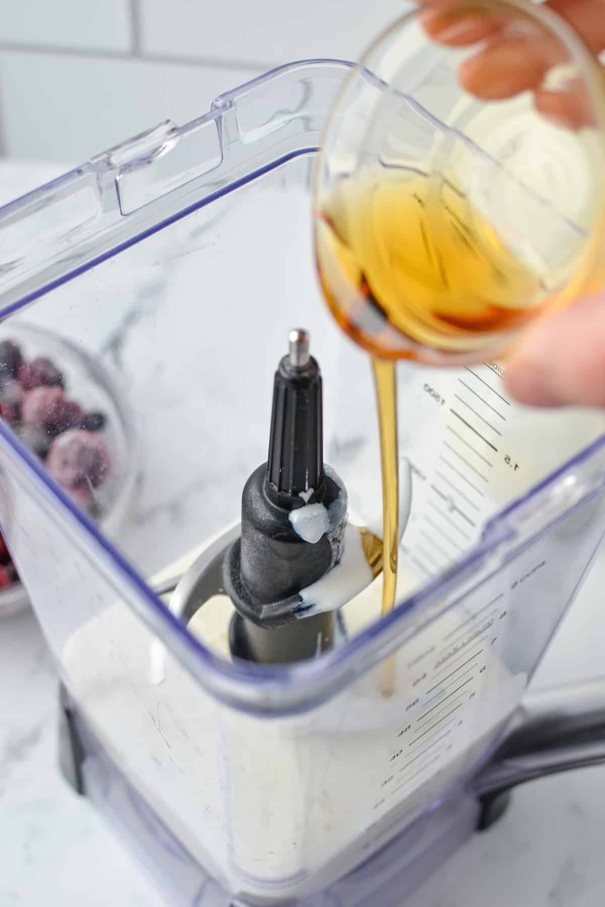 Drizzling maple syrup into a blender with milk kefir.