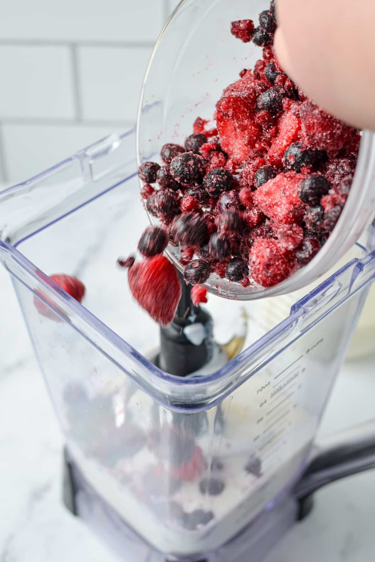Adding frozen fruit to a blender with kefir in it.