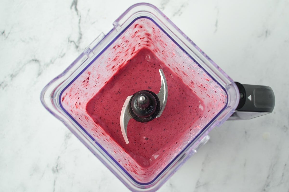 A blender filled with a berry smoothie in it.