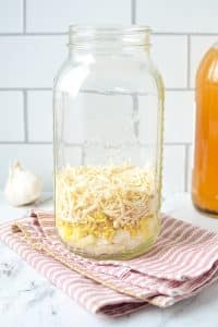 A large mason jar with onions, ginger, and horseradish in the bottom.