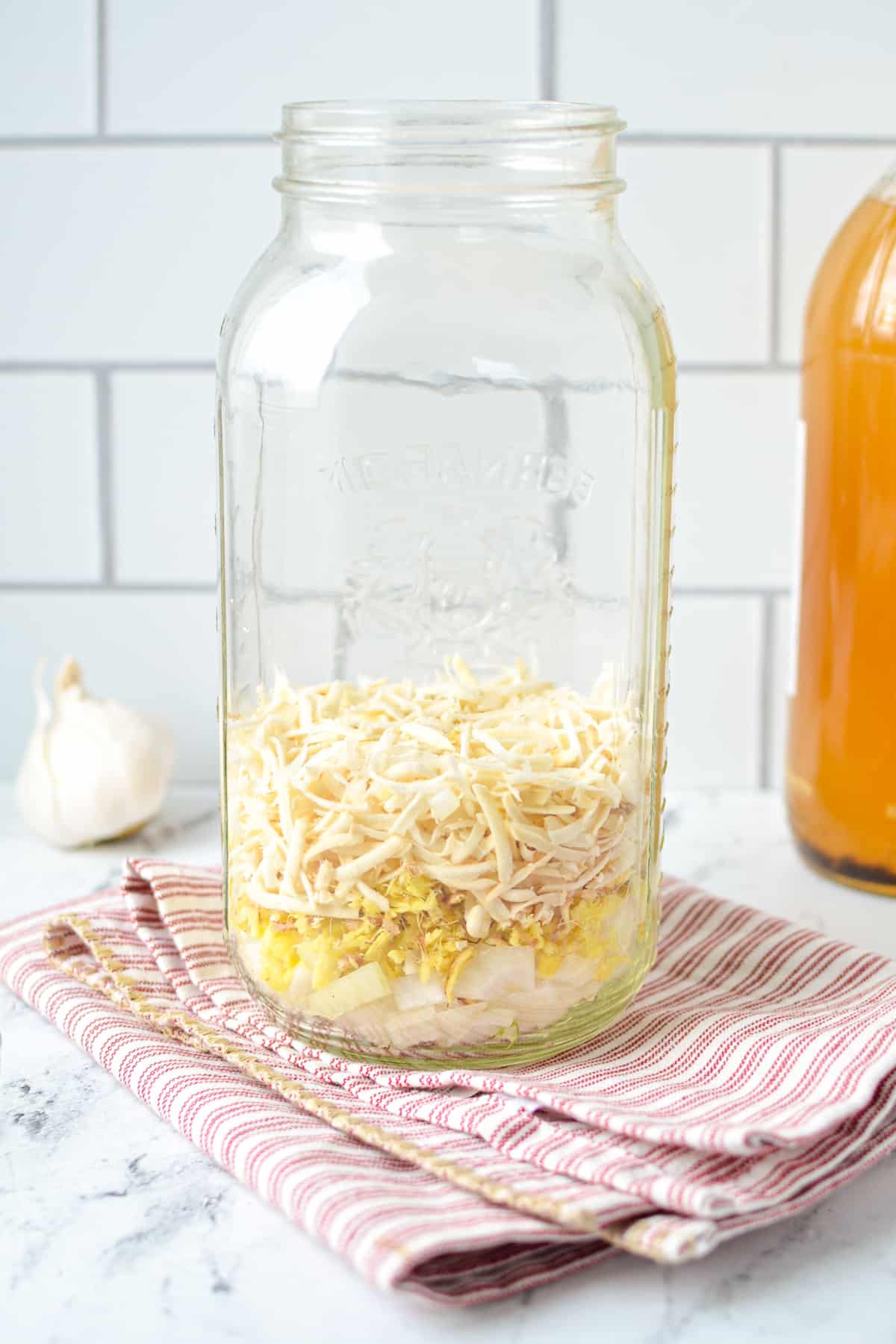 A large mason jar with onions, ginger, and horseradish in the bottom.