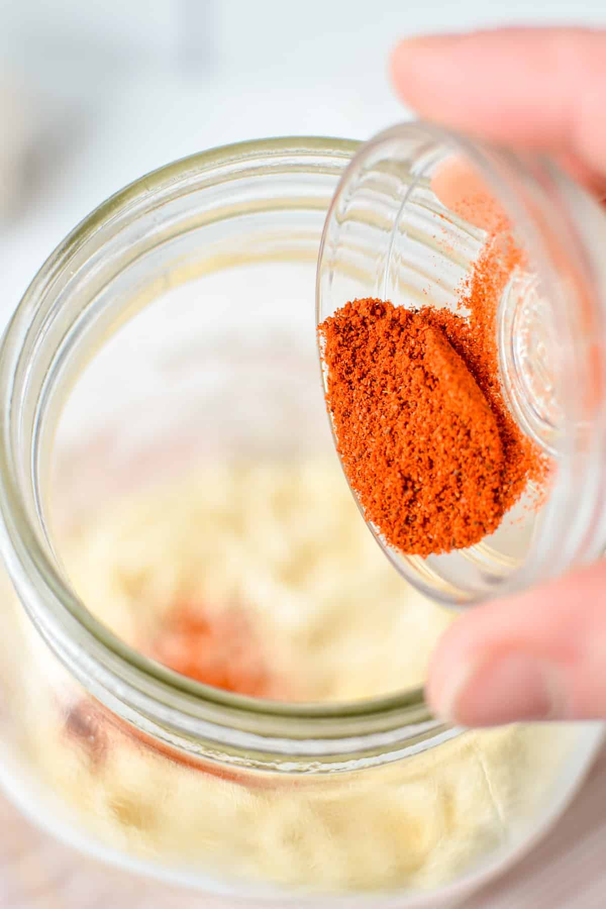 Adding powdered cayenne to a large jar.