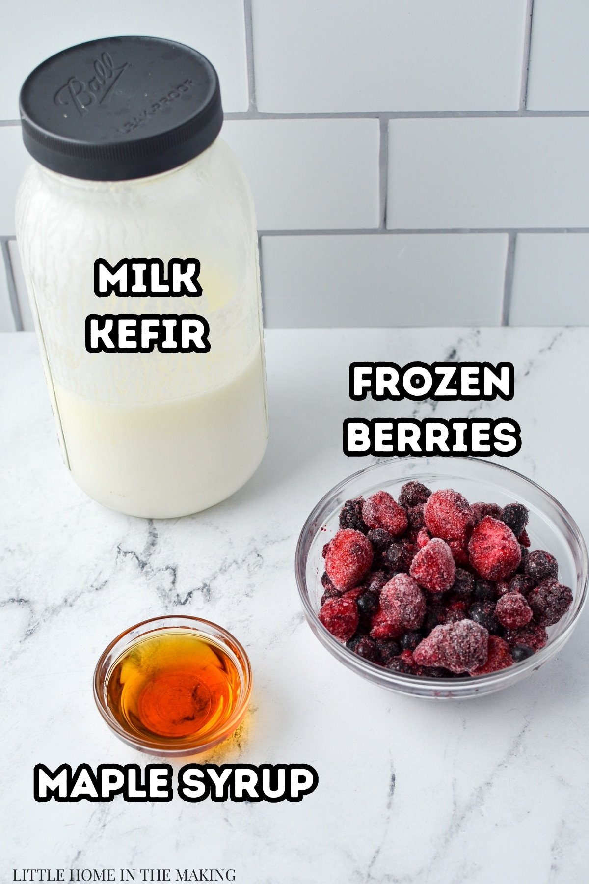 A jar of milk kefir, a bowl of frozen berries, and a small bowl filled with maple syrup.