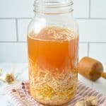 A large mason jar filled with shredded horseradish, ginger, onions, garlic, and apple cider vinegar.