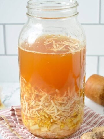A large mason jar filled with shredded horseradish, ginger, onions, garlic, and apple cider vinegar.