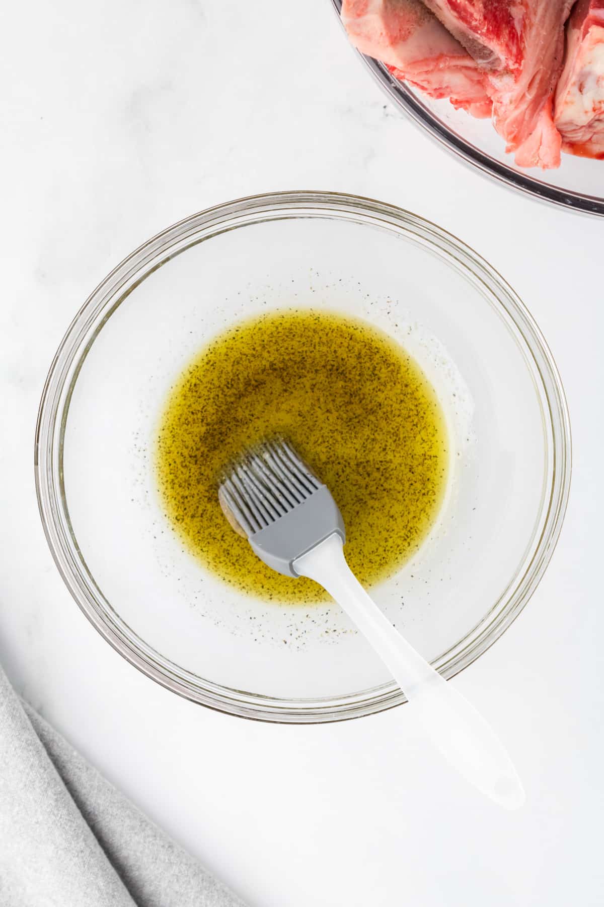 A small bowl filled with olive oil and seasonings with a pastry brush resting on the side.