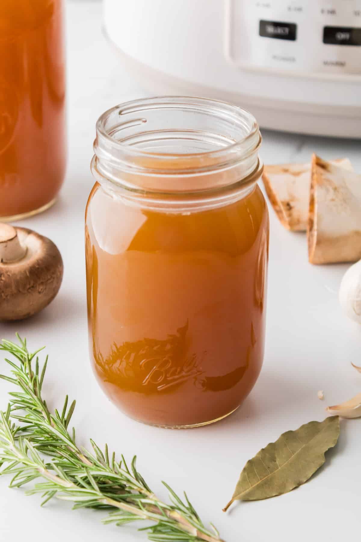 A mason jar filled with beef broth with a slow cooker in the background.
