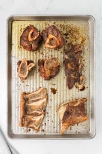 Beef bones on a baking sheet that have been roasted until browned.