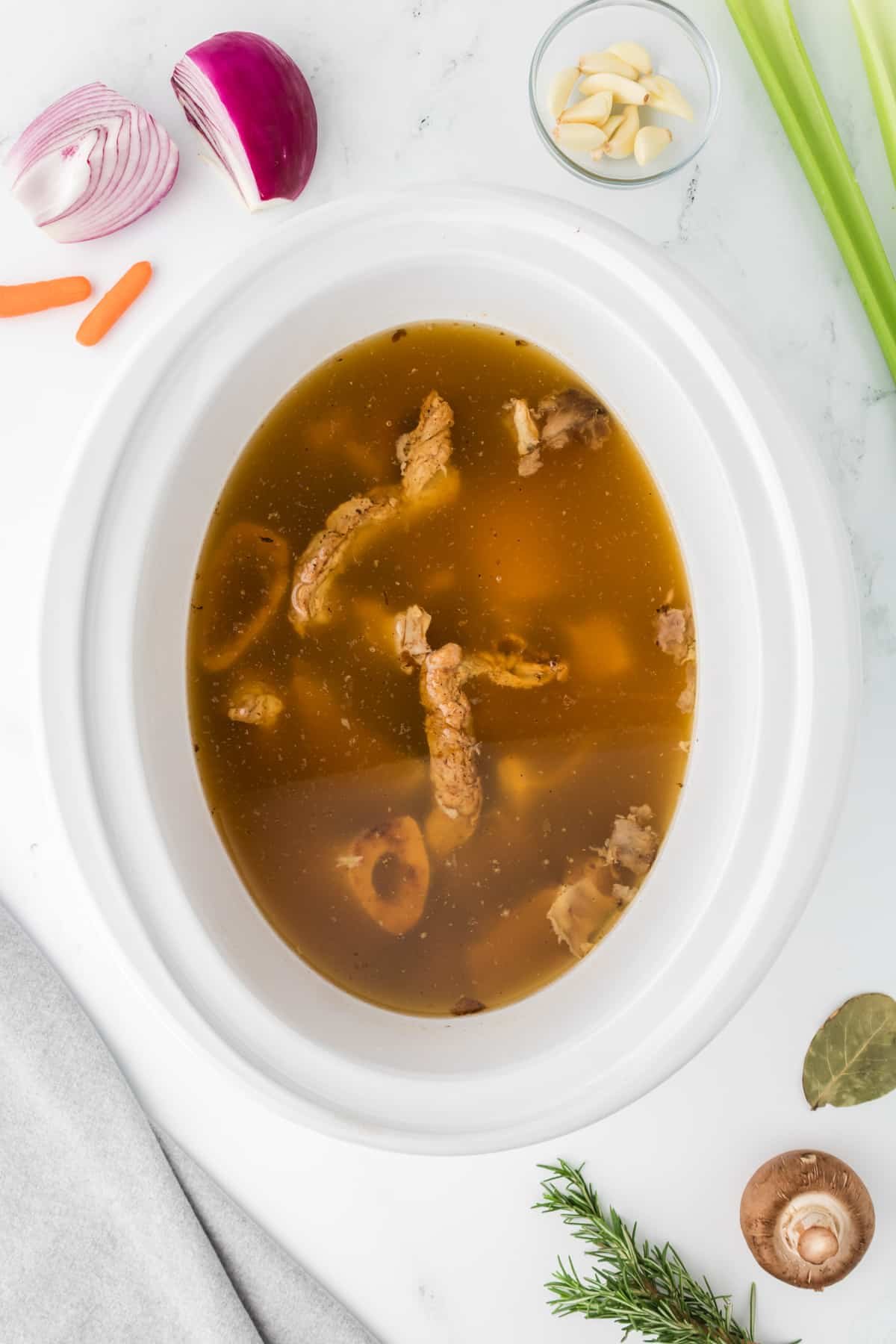 A mix of broth and bones inside of a white slow cooker insert.