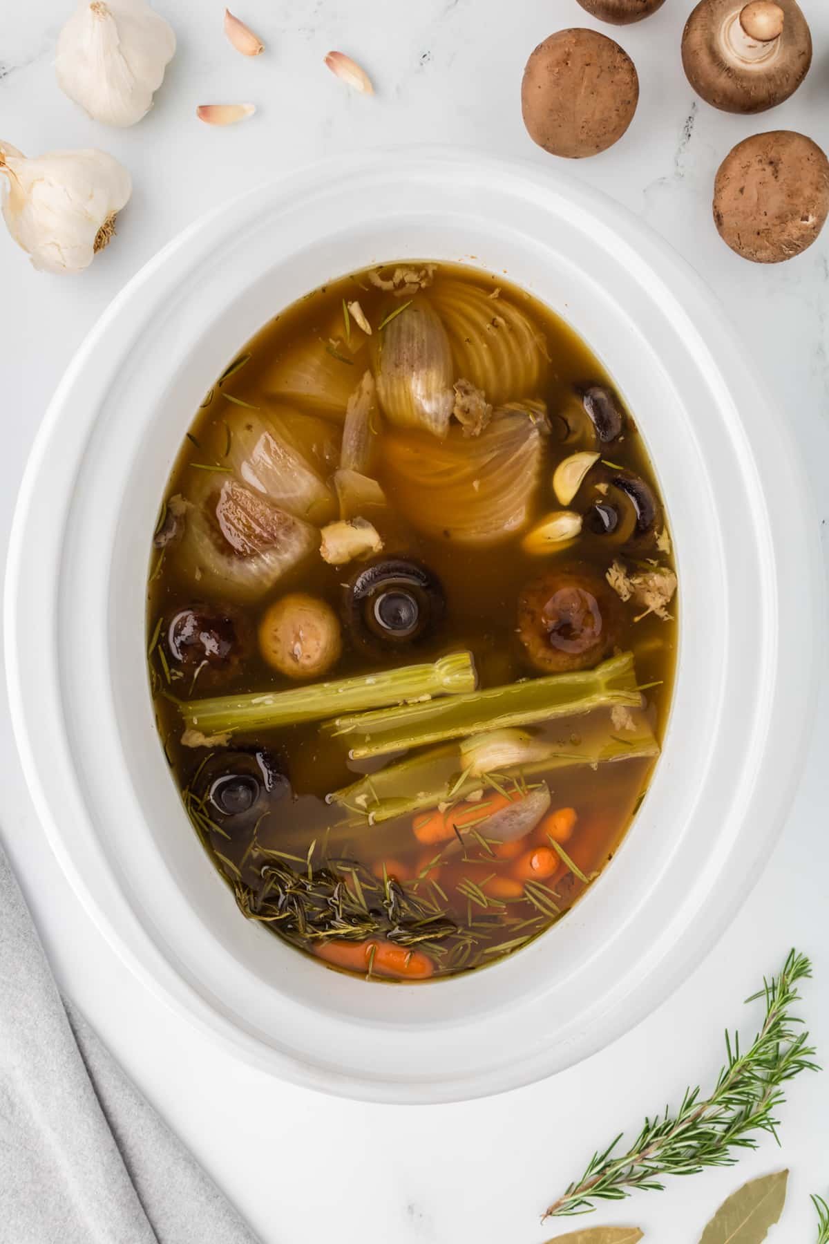 A white slow cooker insert filled with cooked vegetables and broth.