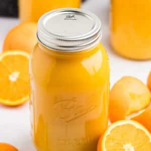 A mason jar filled with orange juice; fresh oranges surround the counter in the background.