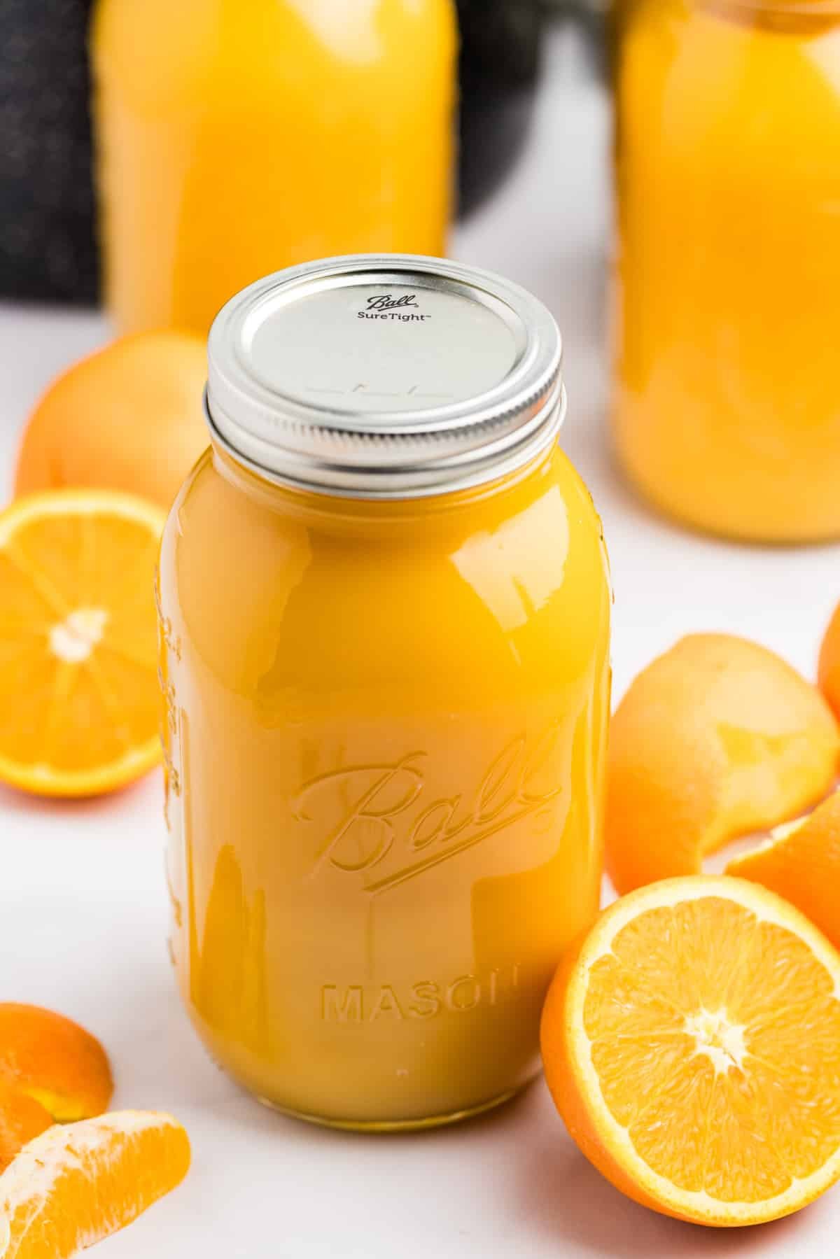 A quart jar filled with orange juice, with some fresh oranges on the counter next to it.