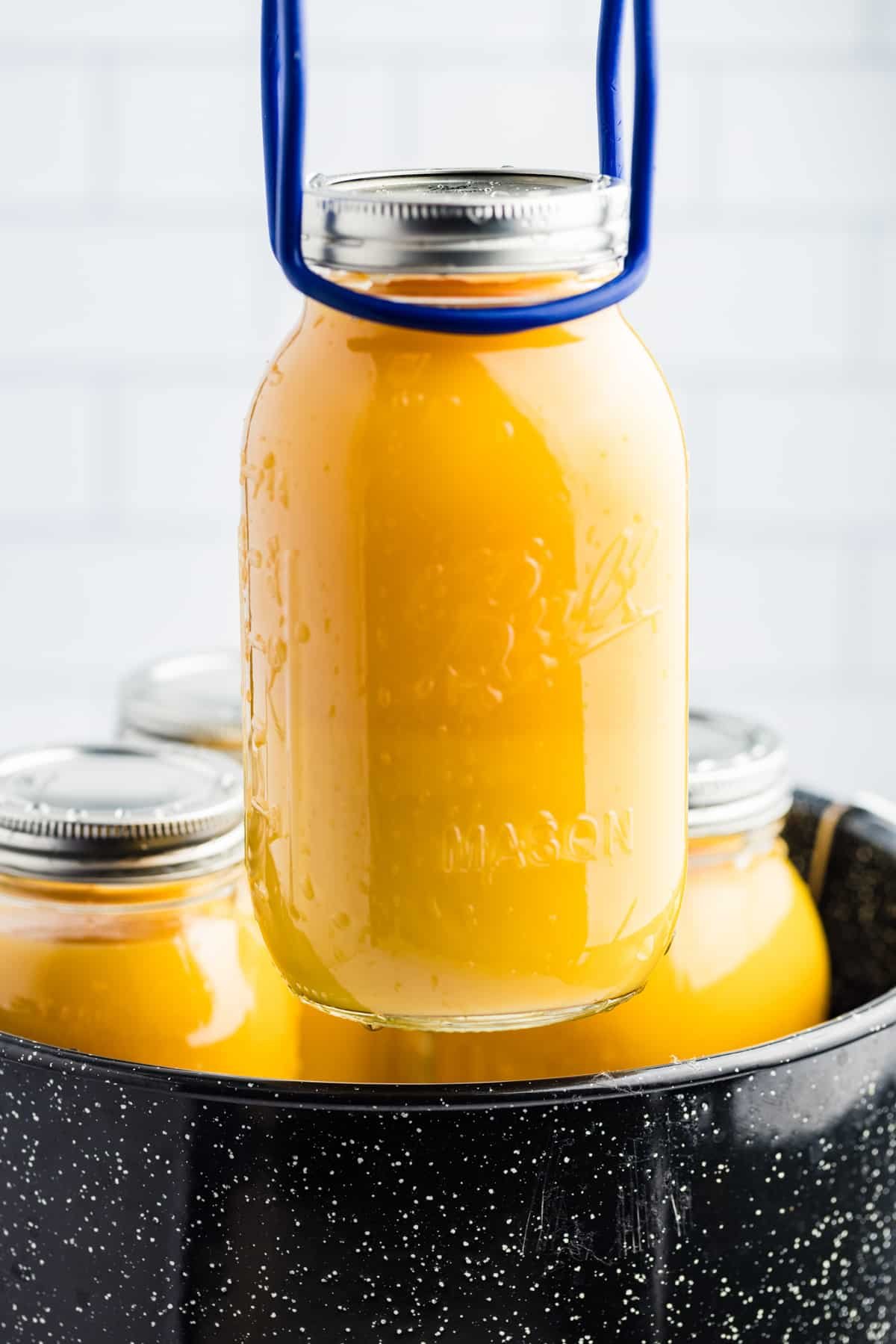 Lifting a quart jar filled with orange juice out of a water bath canner.