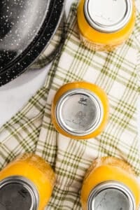 Jars of orange juice resting on a patterned kitchen towel.