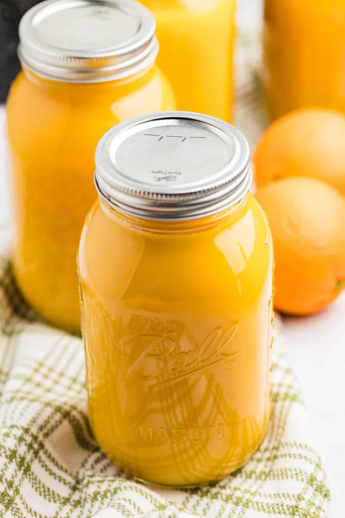 A large canning jar filled with citrus juice, with fresh oranges in the background.