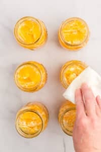 Wiping the rim of canning jars filled with orange segments.