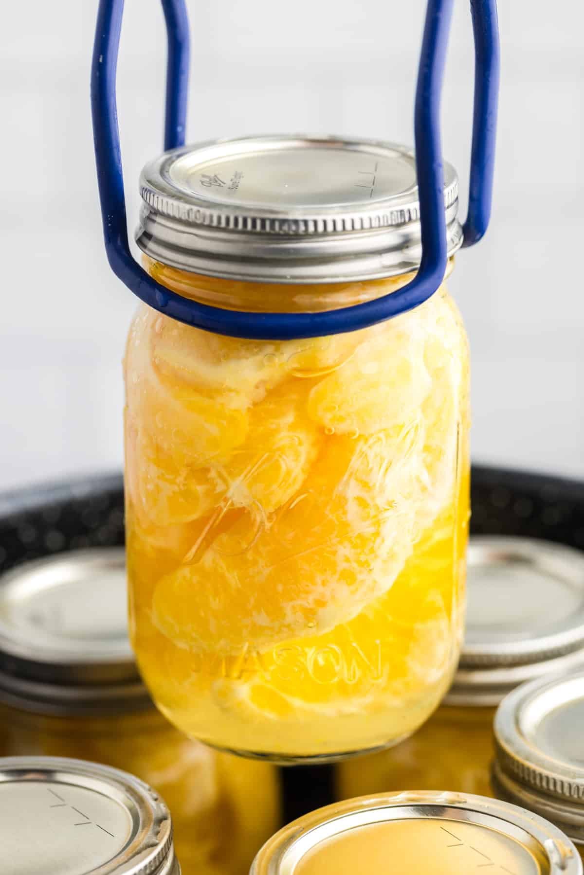 Lifting a jar of home canned oranges from a canning pot.