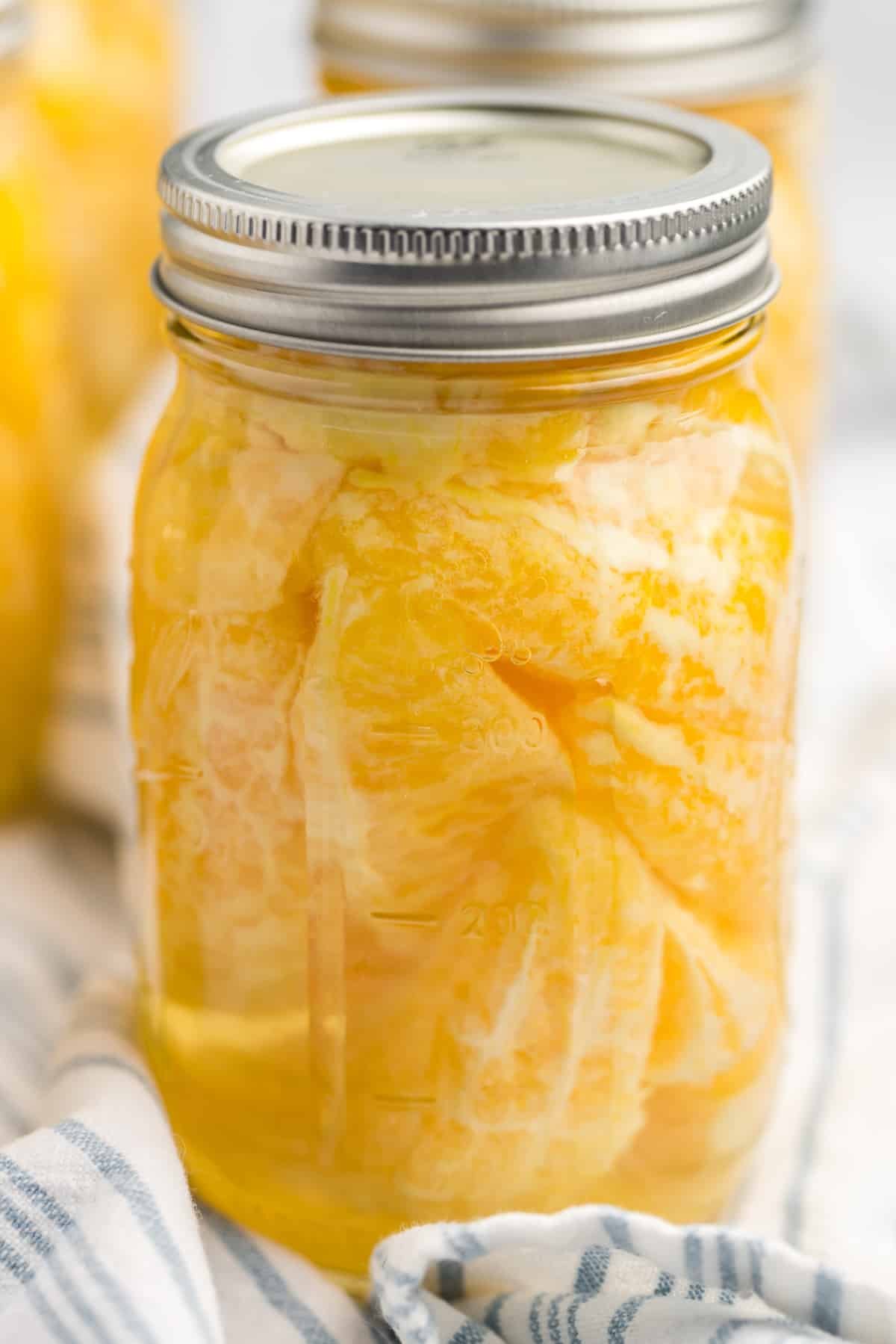 A canning jar with oranges encased in a liquid.