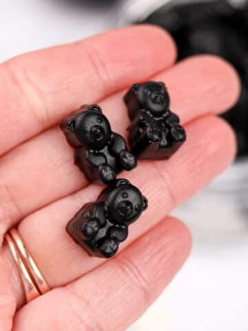 A hand holding gummy bears that are dark in color.