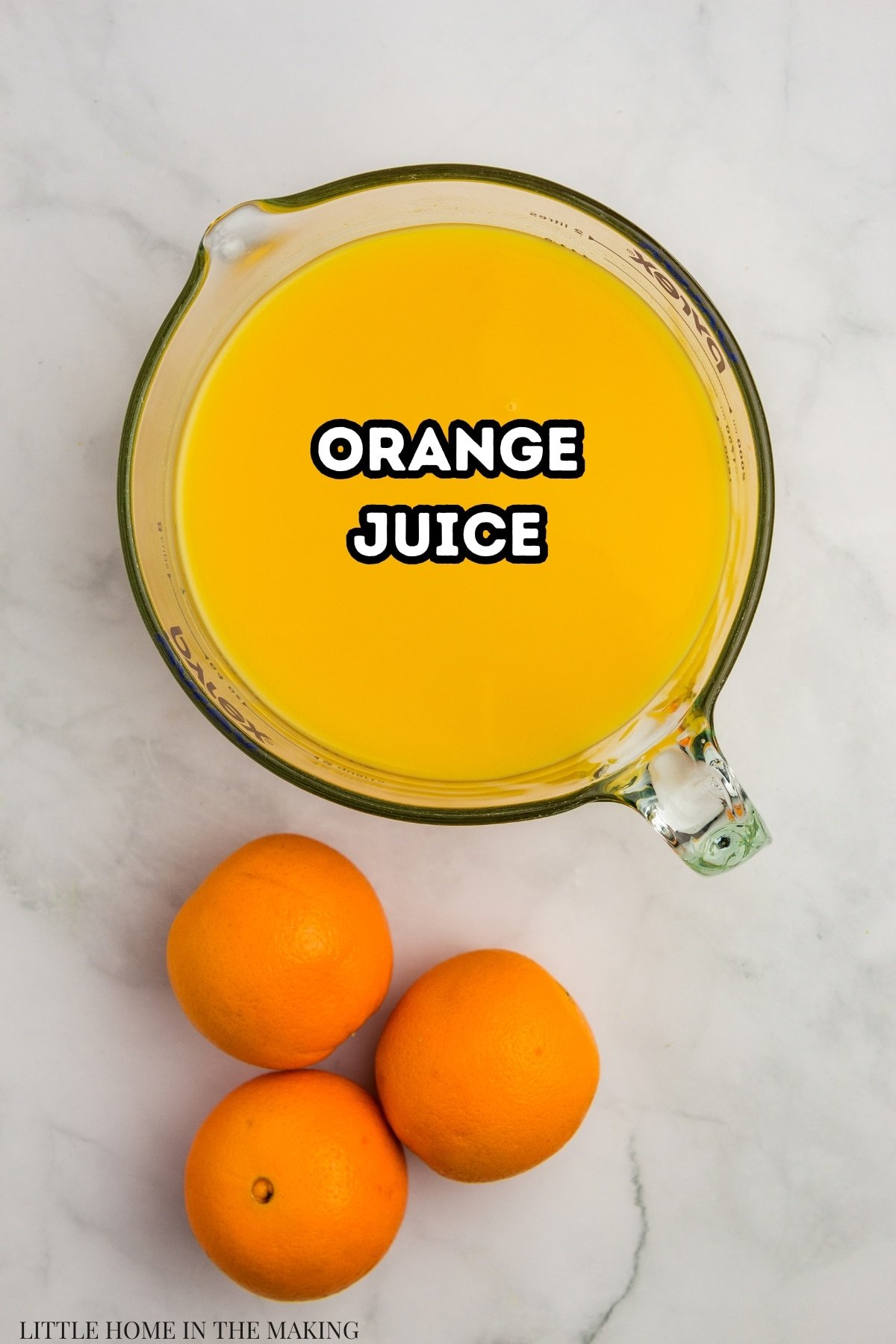 A large measuring cup of orange juice, with 3 oranges next to it on the counter.