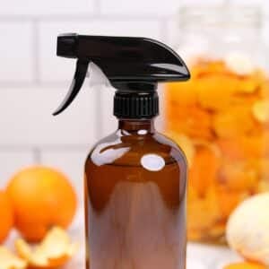 An amber glass spray bottle with oranges in the background.