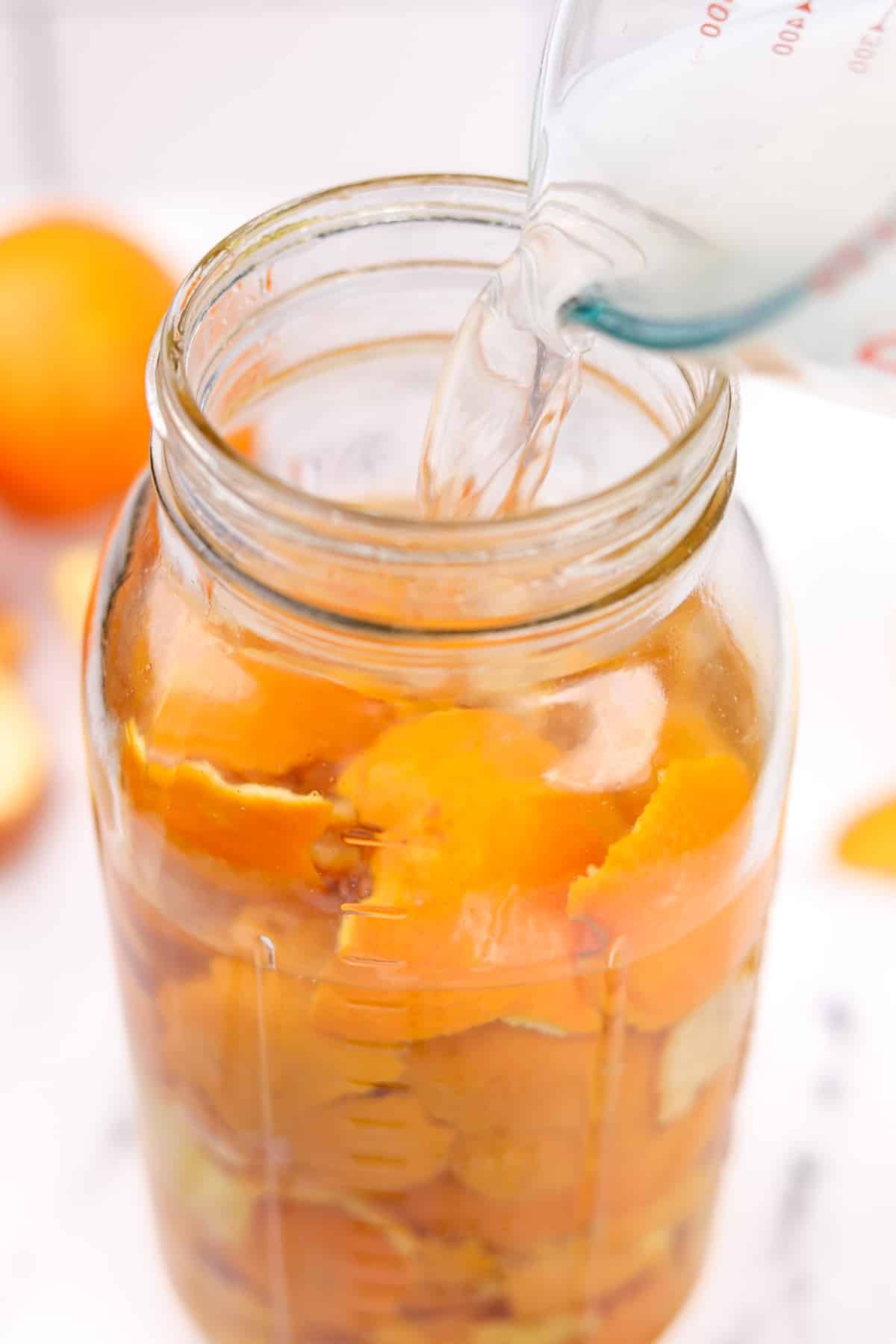 Pouring vinegar into a jar of orange peels.