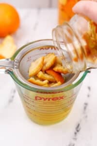 Pouring a jar of orange peels and vinegar through a strainer.