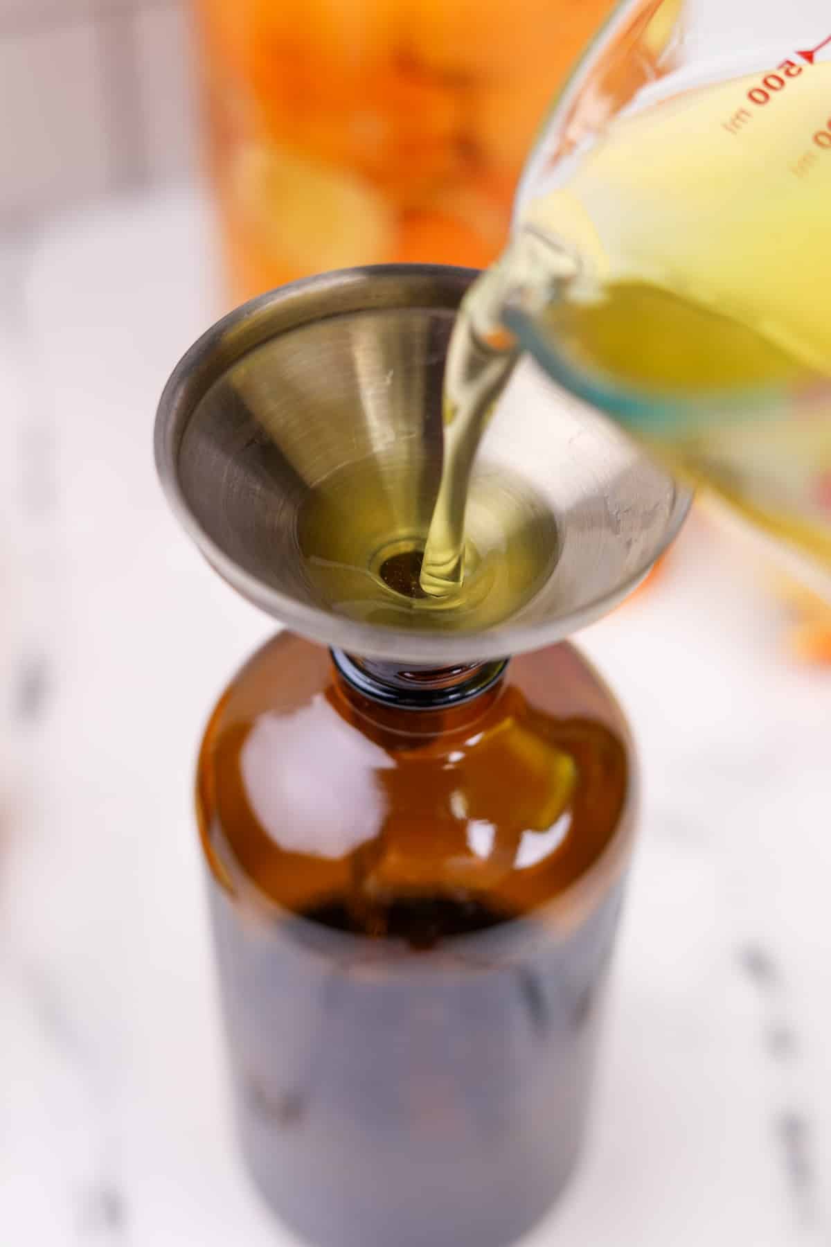 Pouring orange vinegar through a funnel into an amber glass bottle.