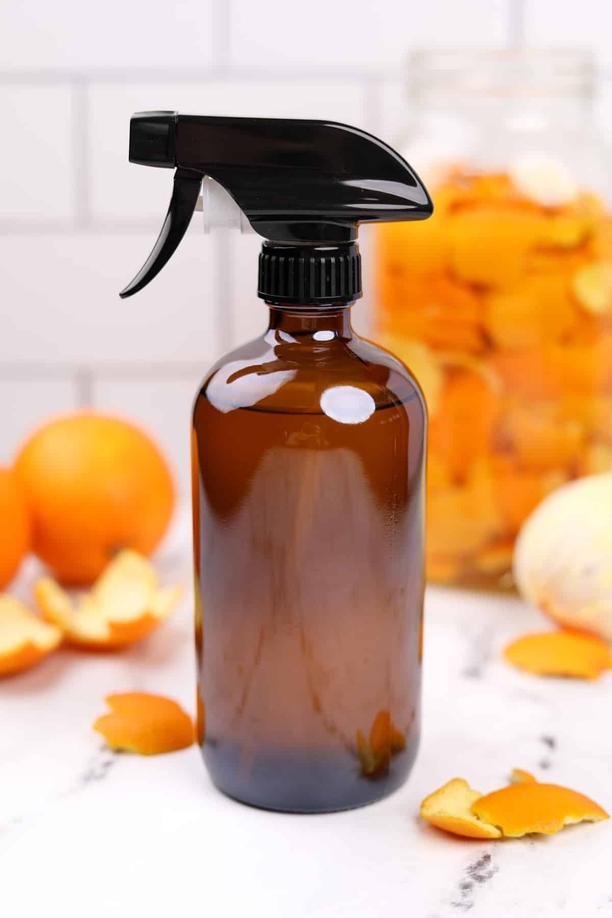A glass bottle with orange peels and oranges in the background.