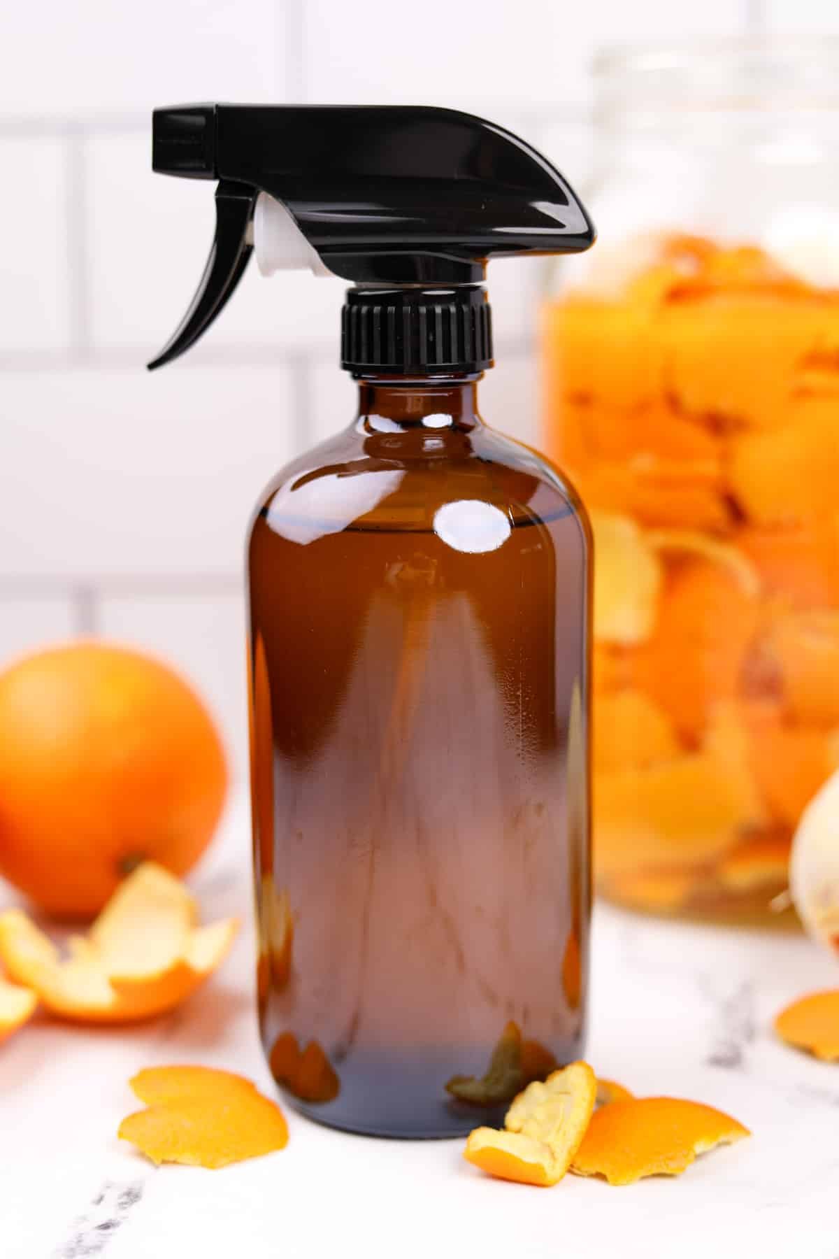 An amber glass spray bottle with whole oranges all around.