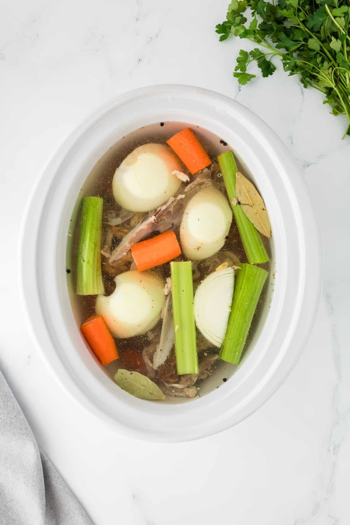 A crock pot filled with water, vegetables, and bones.