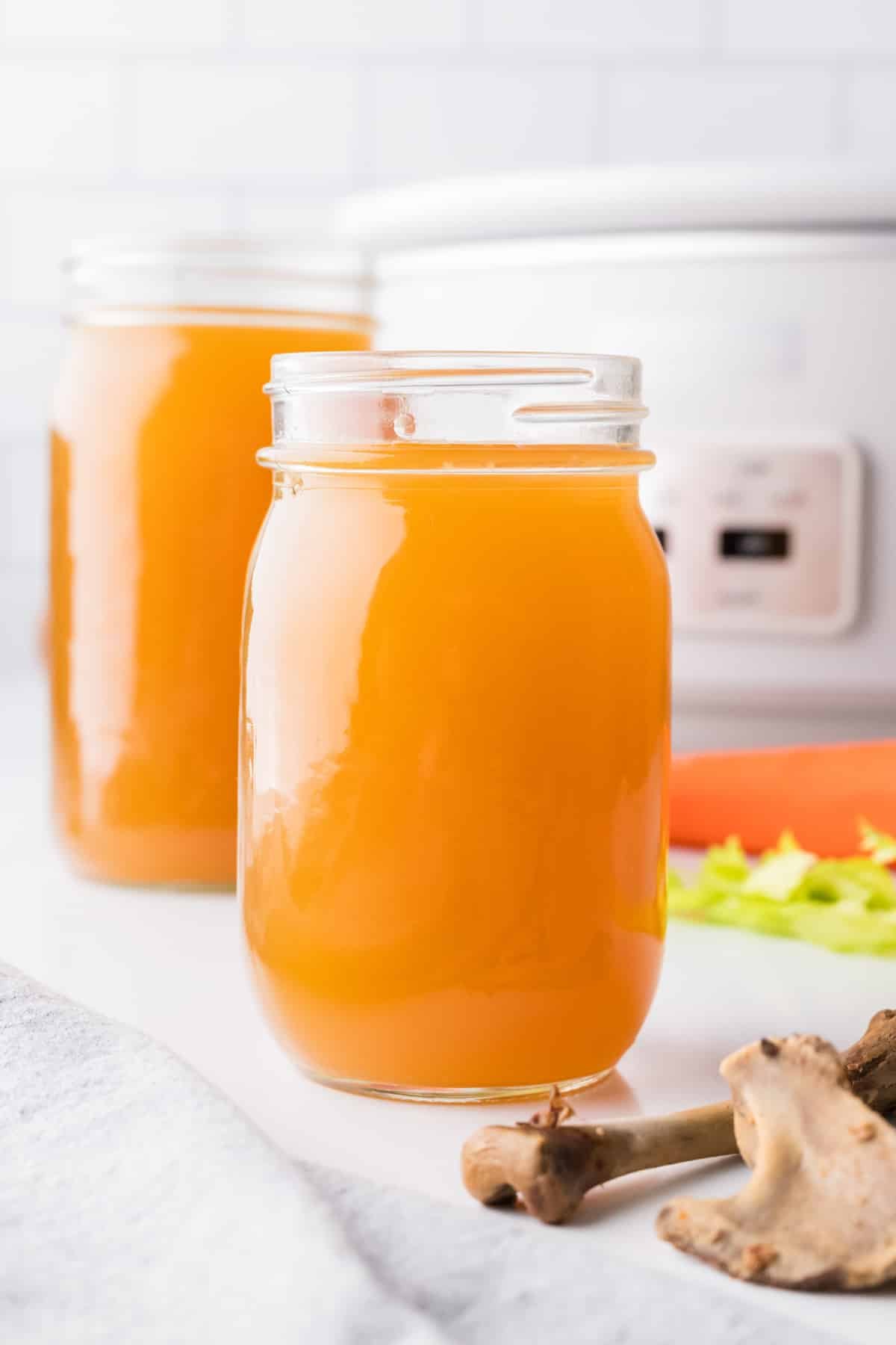 Glass canning jars filled with bone broth, with a slow cooker in the background.