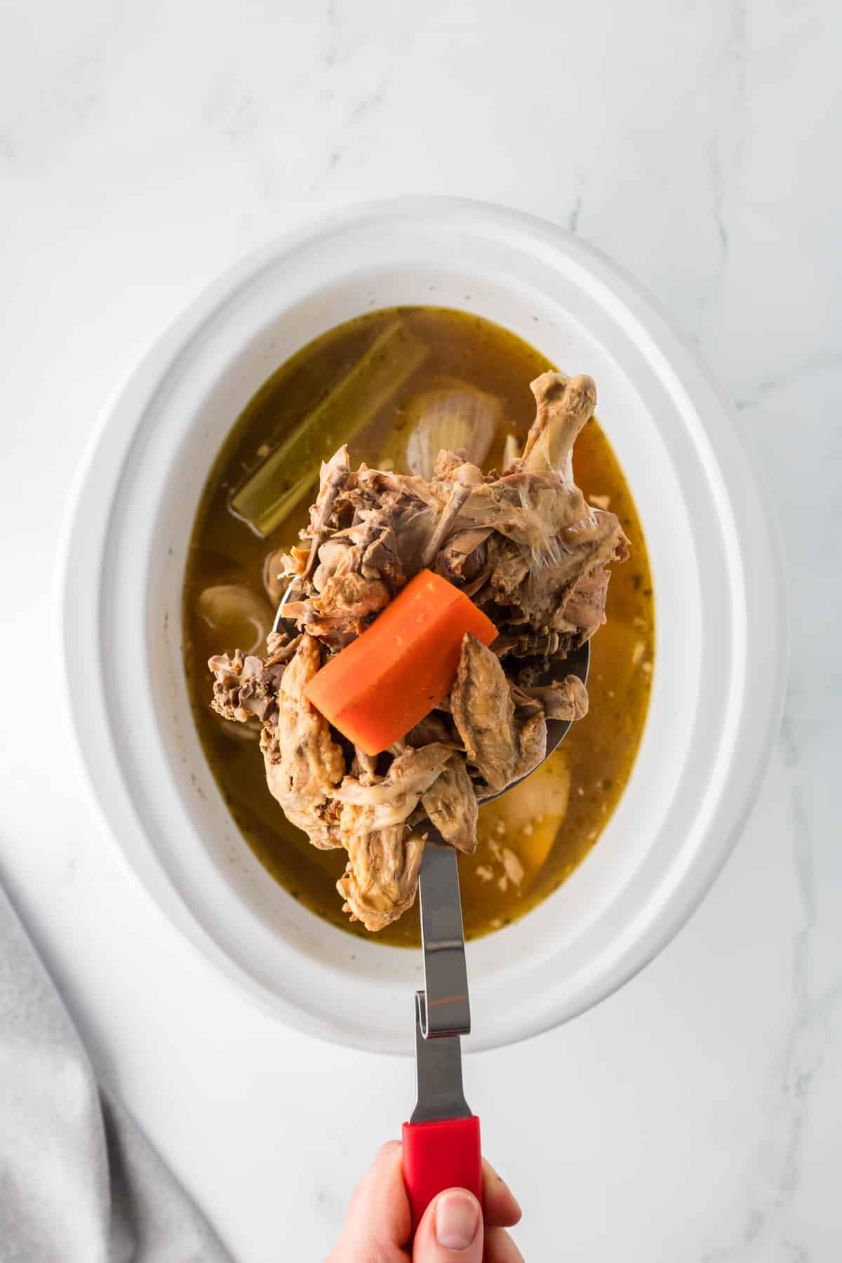 Lifting the solids from a batch of broth using a ladle.