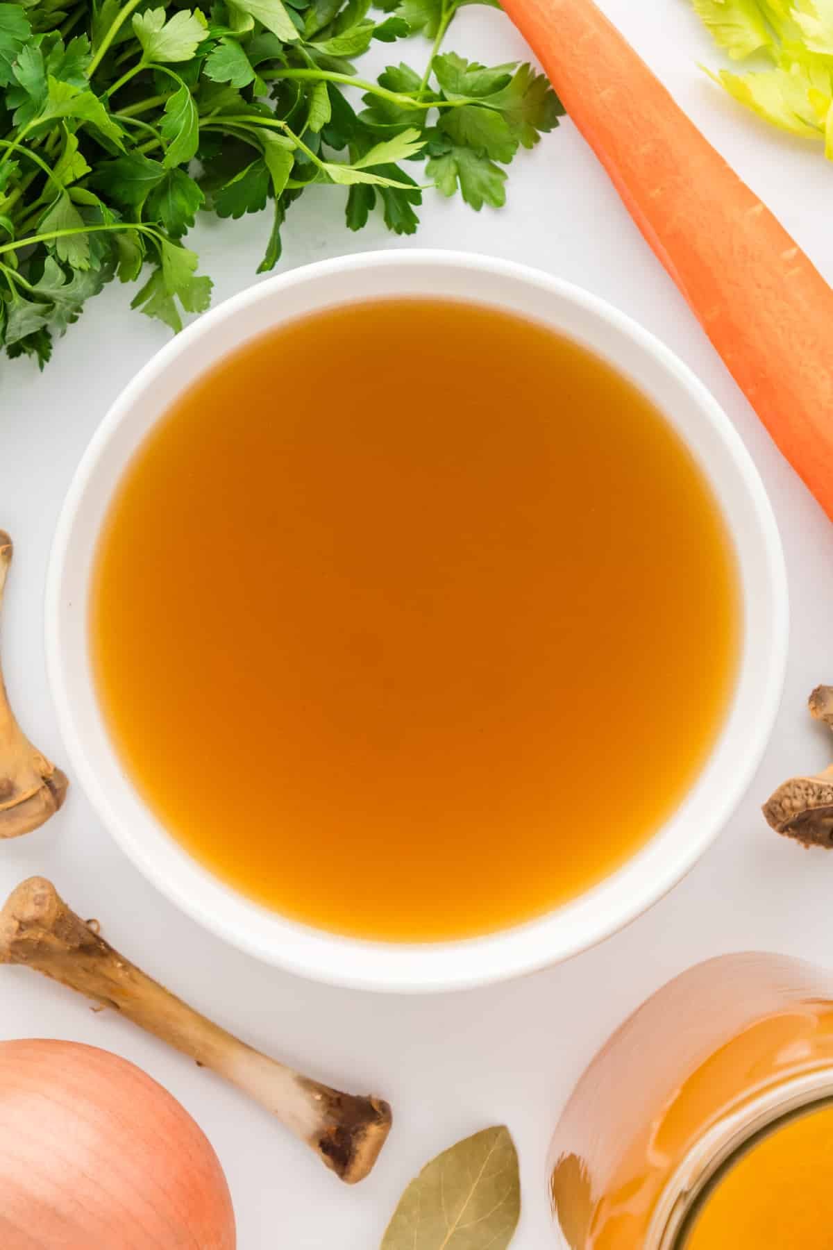 A bowl filled with broth, with vegetables around the outside of the bowl.