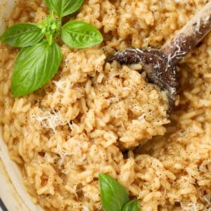 A wooden spoon taking a scoop of risotto from a dish.