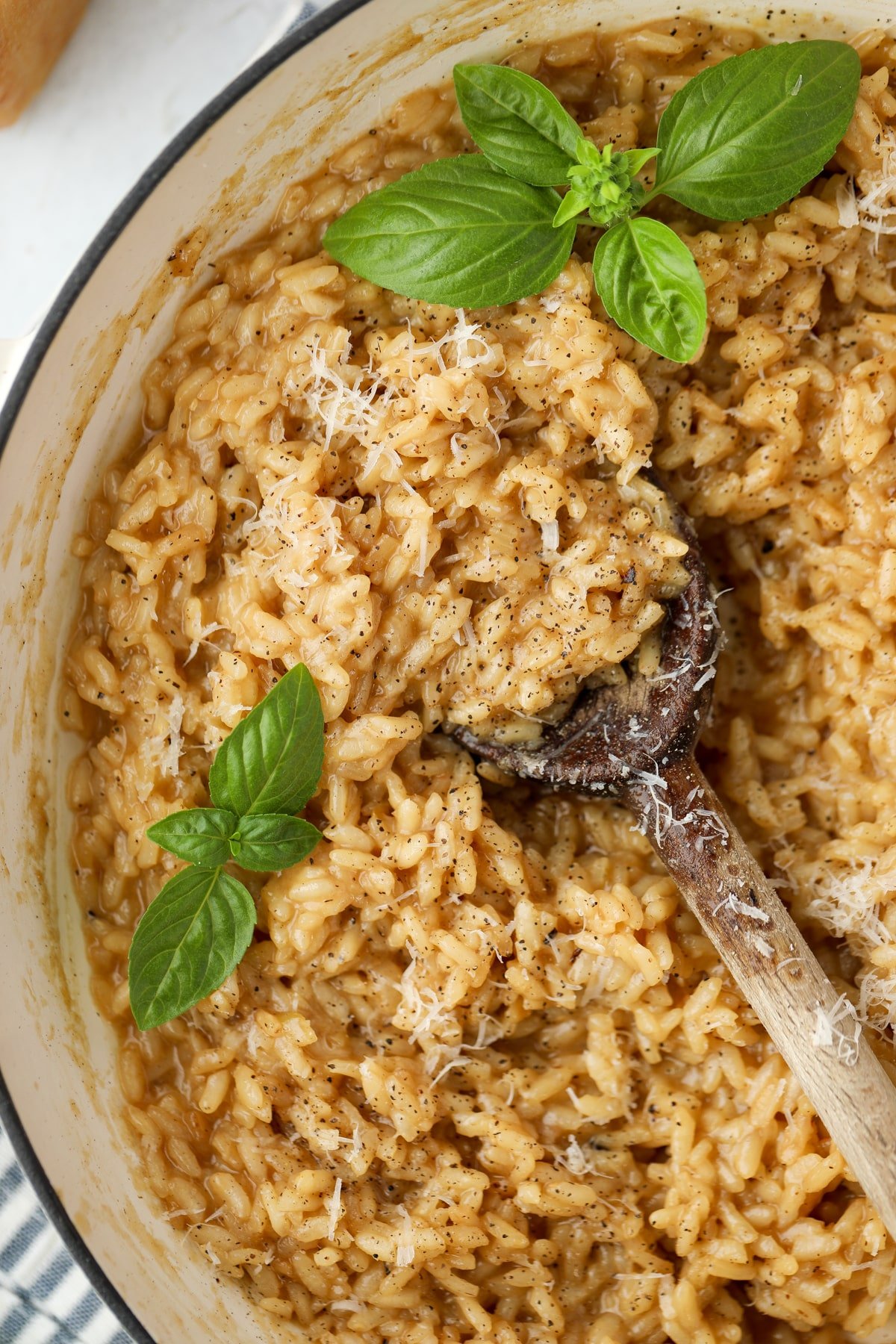 A skillet filled with risotto, with a wooden spoon taking a scoop.