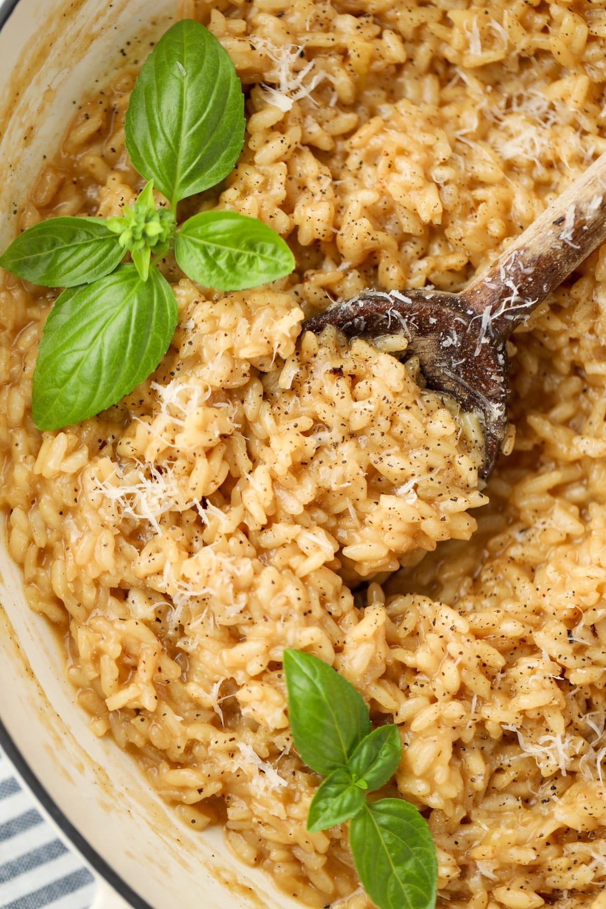 A wooden spoon serving up a portion of risotto garnished with basil.