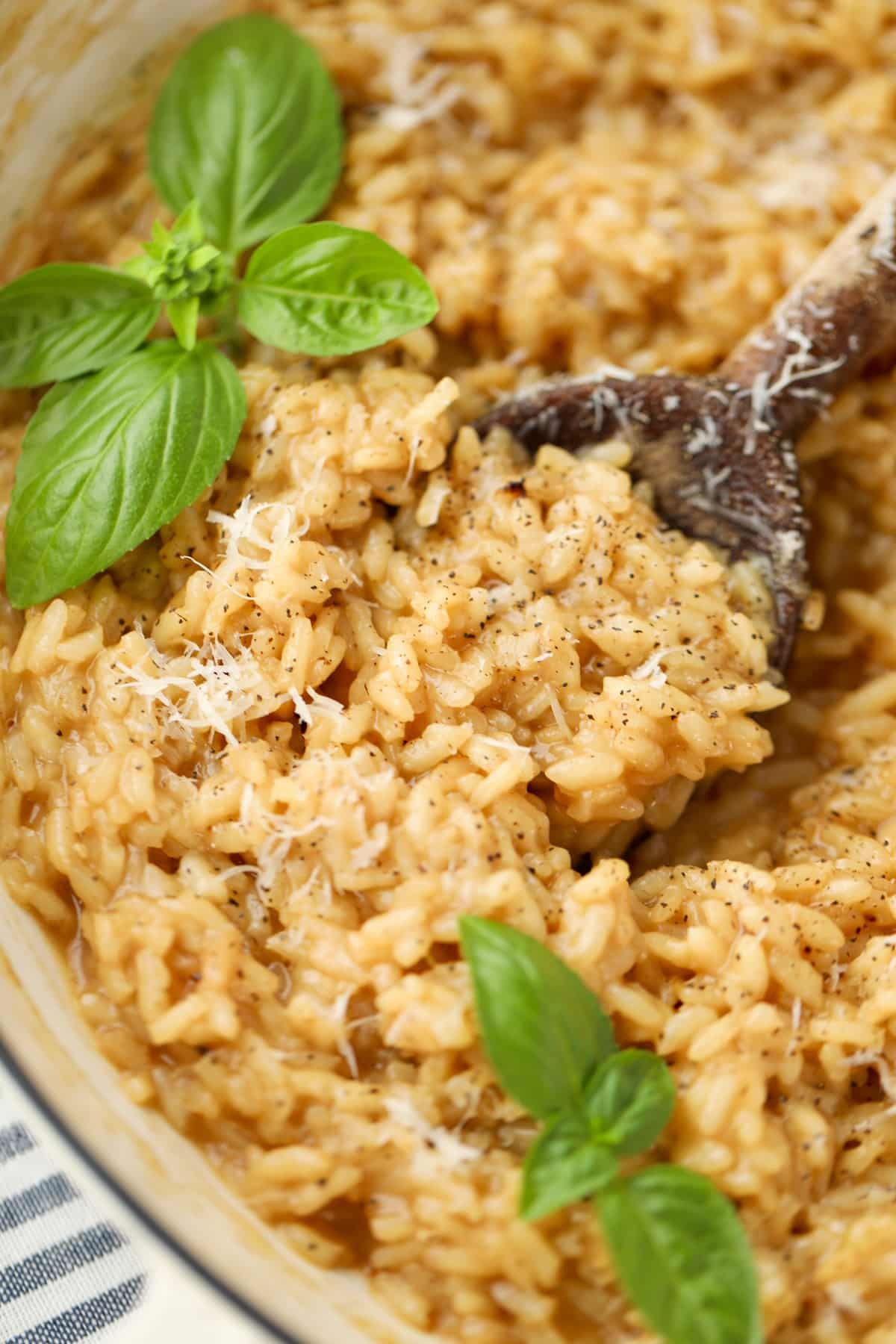 A wooden spoon taking a portion of risotto from a skillet.