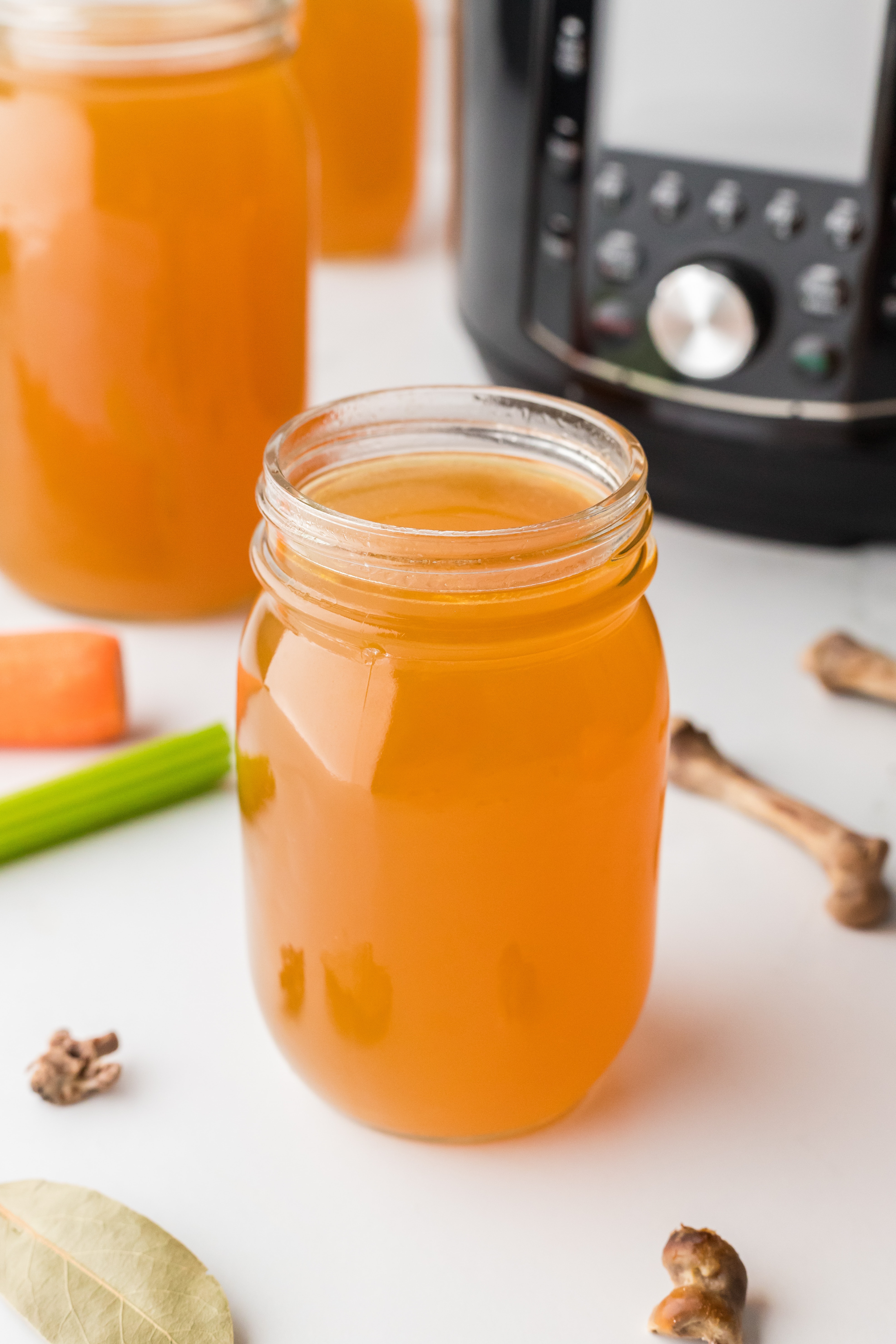 A glass jar filled with broth in front of an Instant Pot.