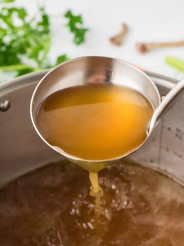 A ladle of bone broth lifting from a large Instant Pot insert.