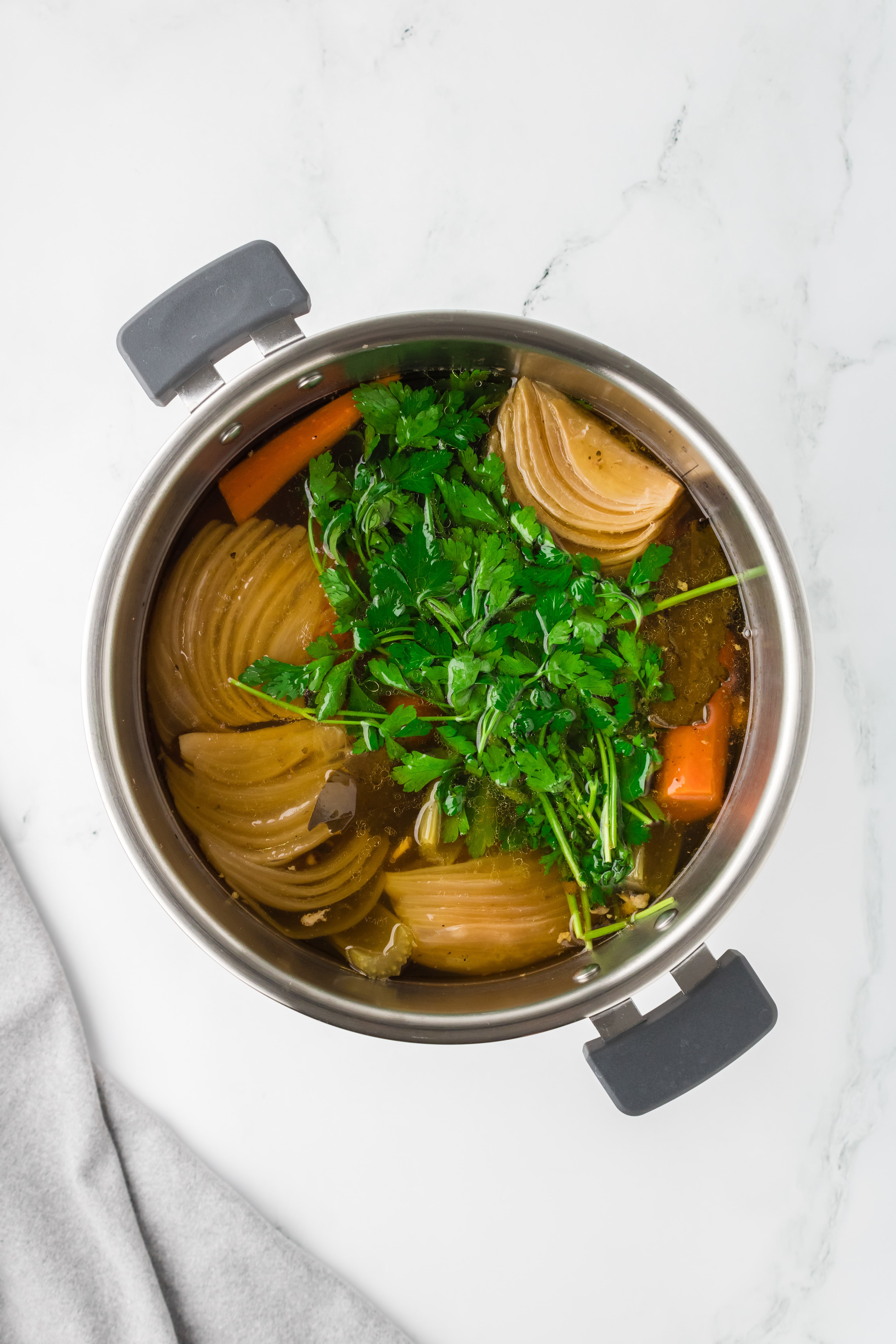 An Instant Pot insert filled with broth, with a bunch of parsley floating on top.