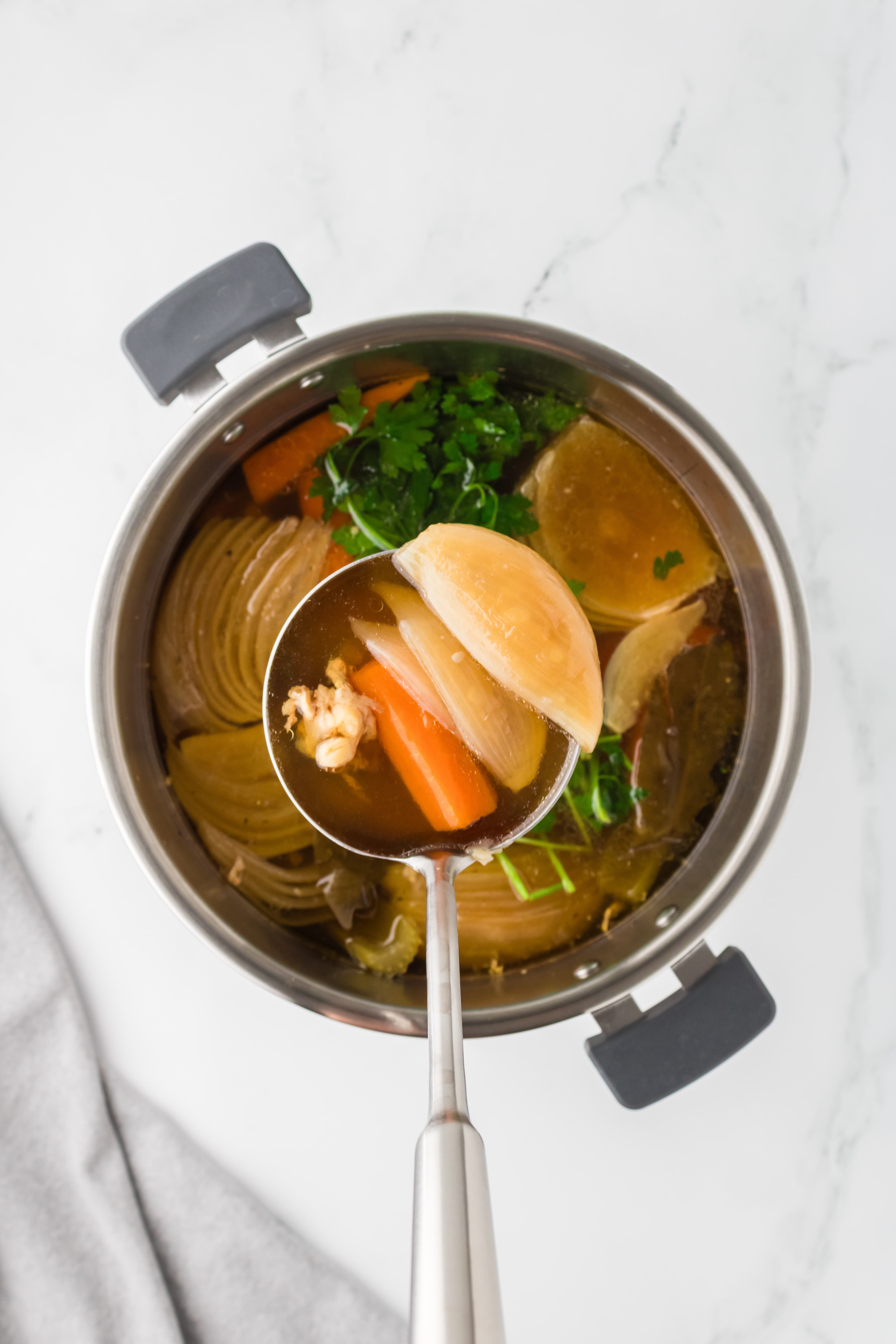 A ladle lifting vegetables from a pot of broth.