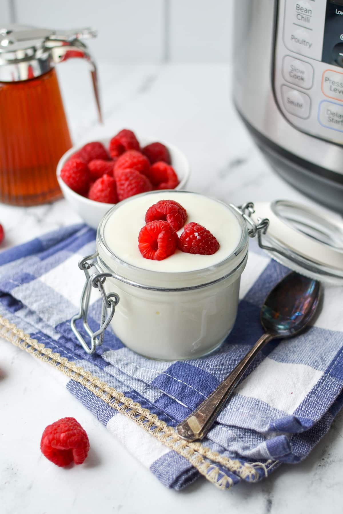 A small glass jar filled with yogurt and topped with fresh raspberries.