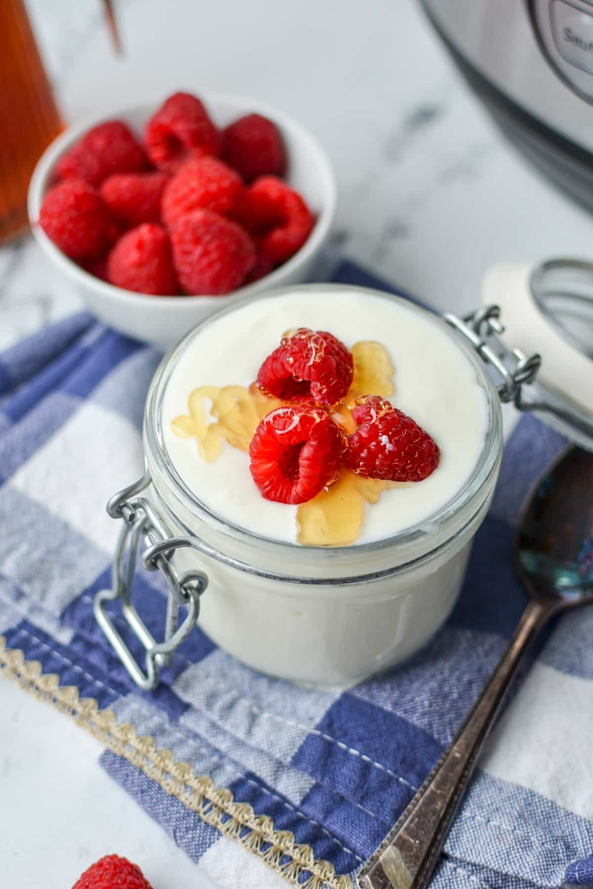 A glass jar filled with yogurt, and topped with raspberries and honey.