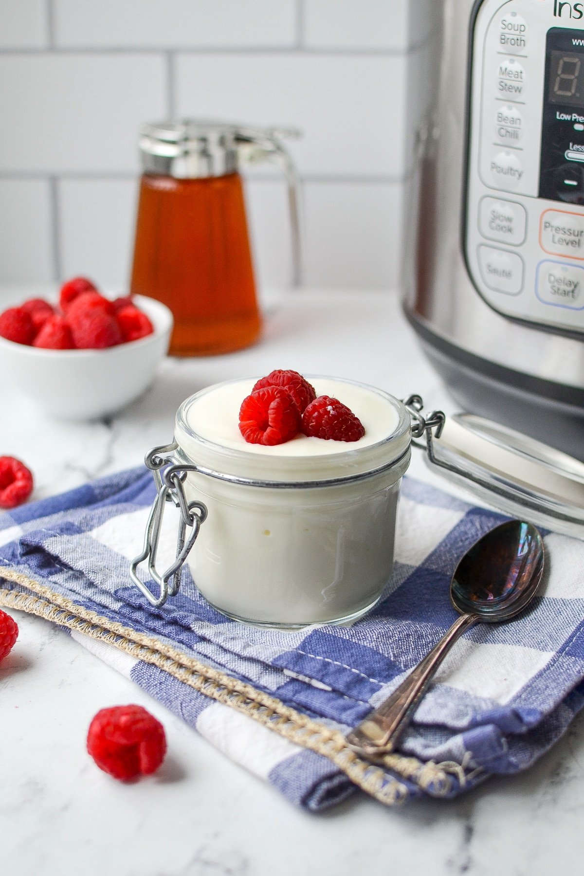 A small glass jar filled with yogurt and topped with fresh raspberries.