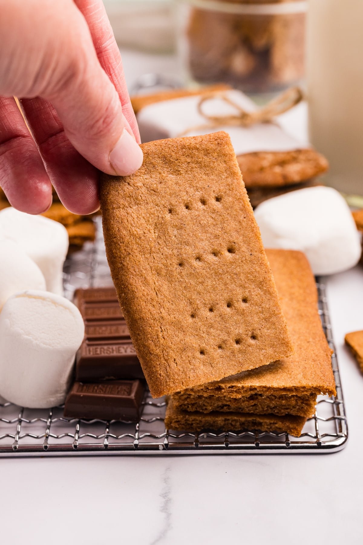 Taking a small graham cracker off of a pile of several on a wire cooling rack.