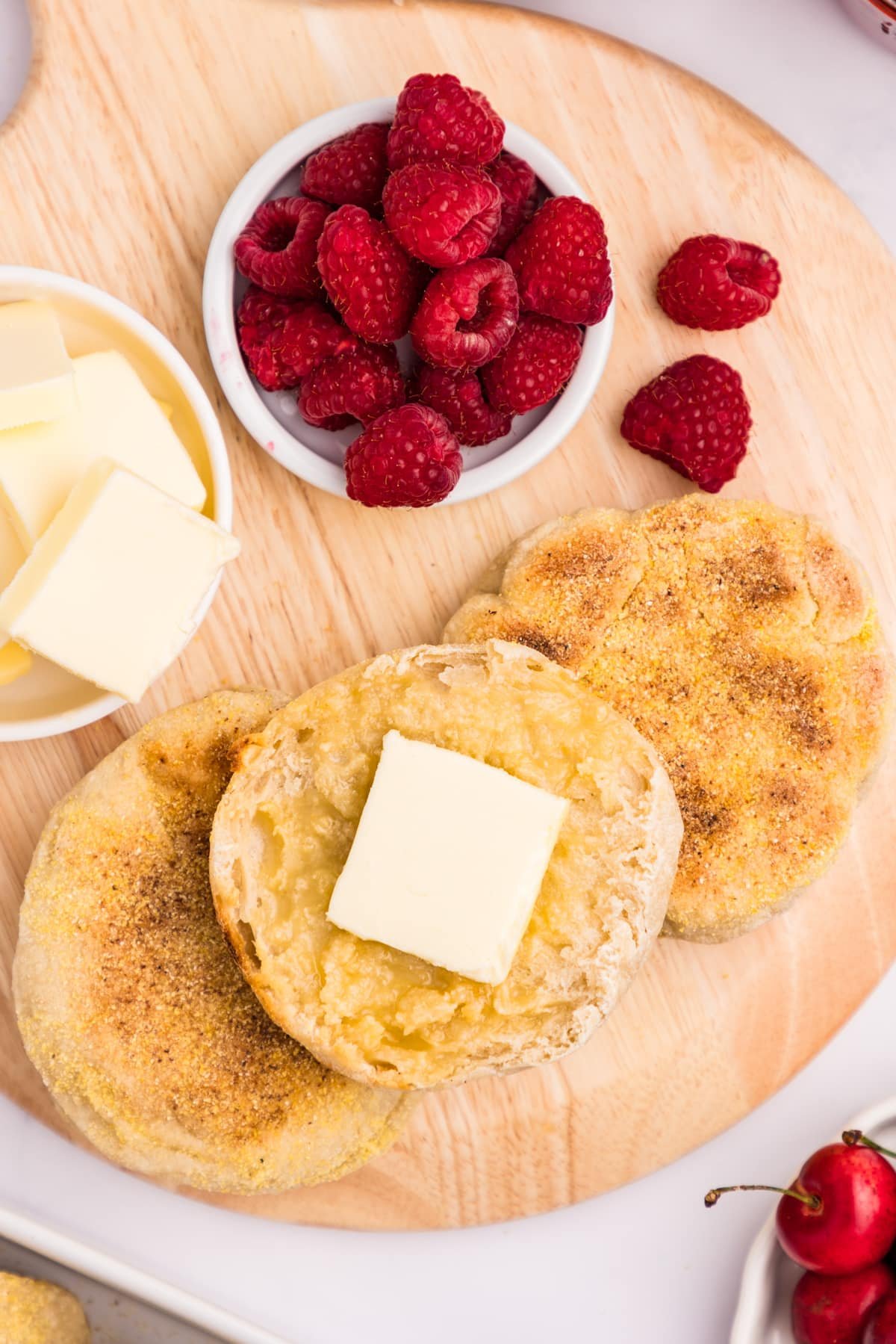 Split english muffins topped with butter, with a small bowl of raspberries on the side.