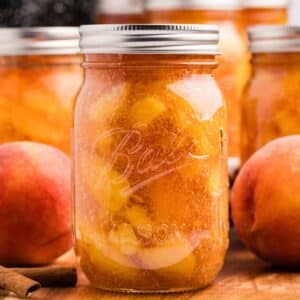 A jar of peach pie filling surrounded by other jars and fresh peaches.