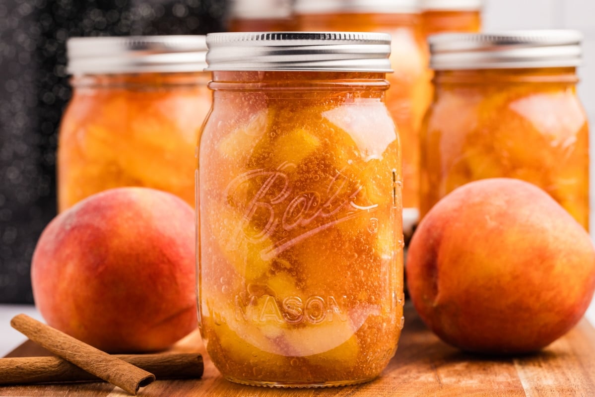 Jars of preserved peach filling surrounded by fresh peaches.